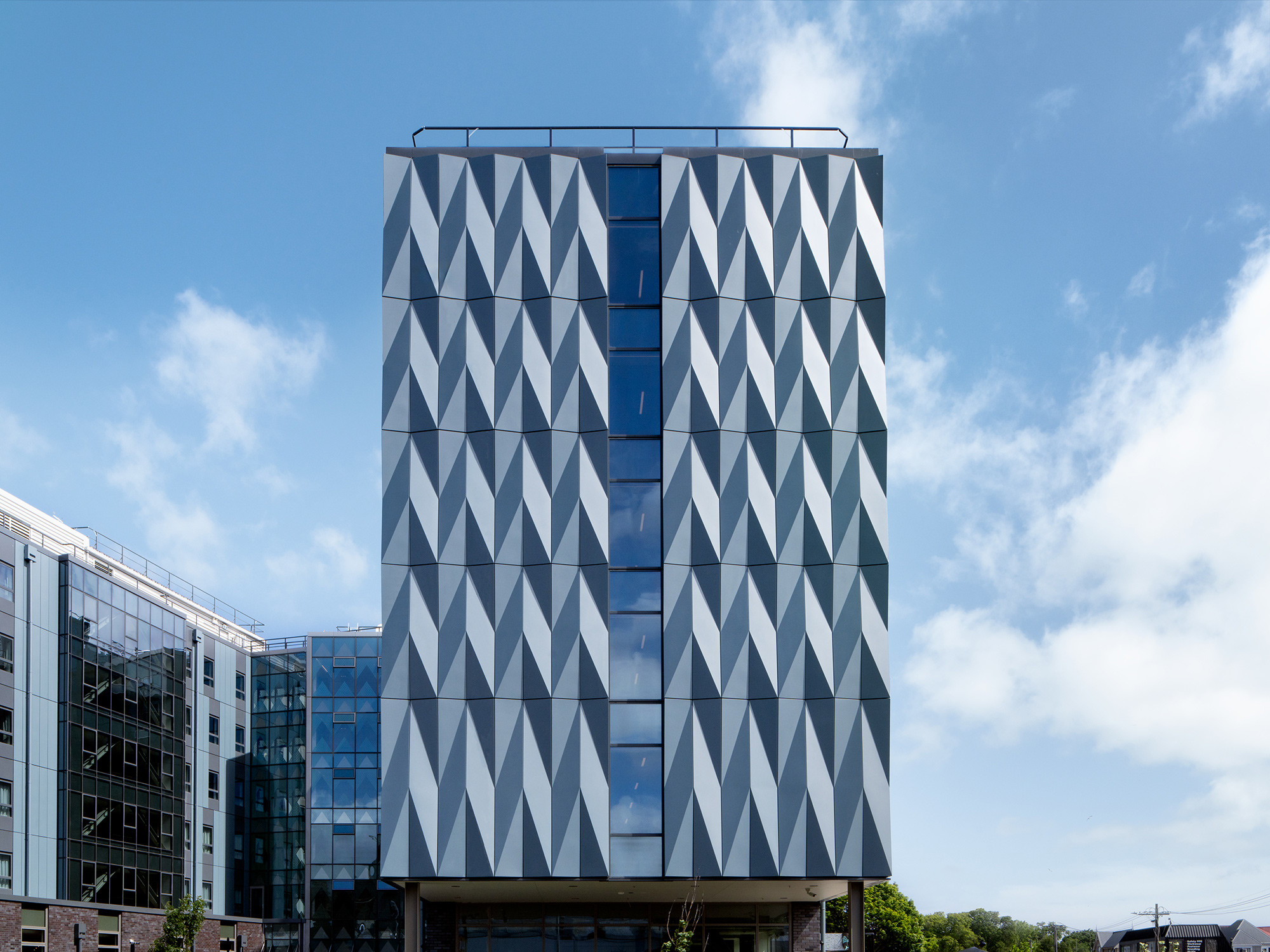 A tall building with a triangular design on the side, featuring glass canopies