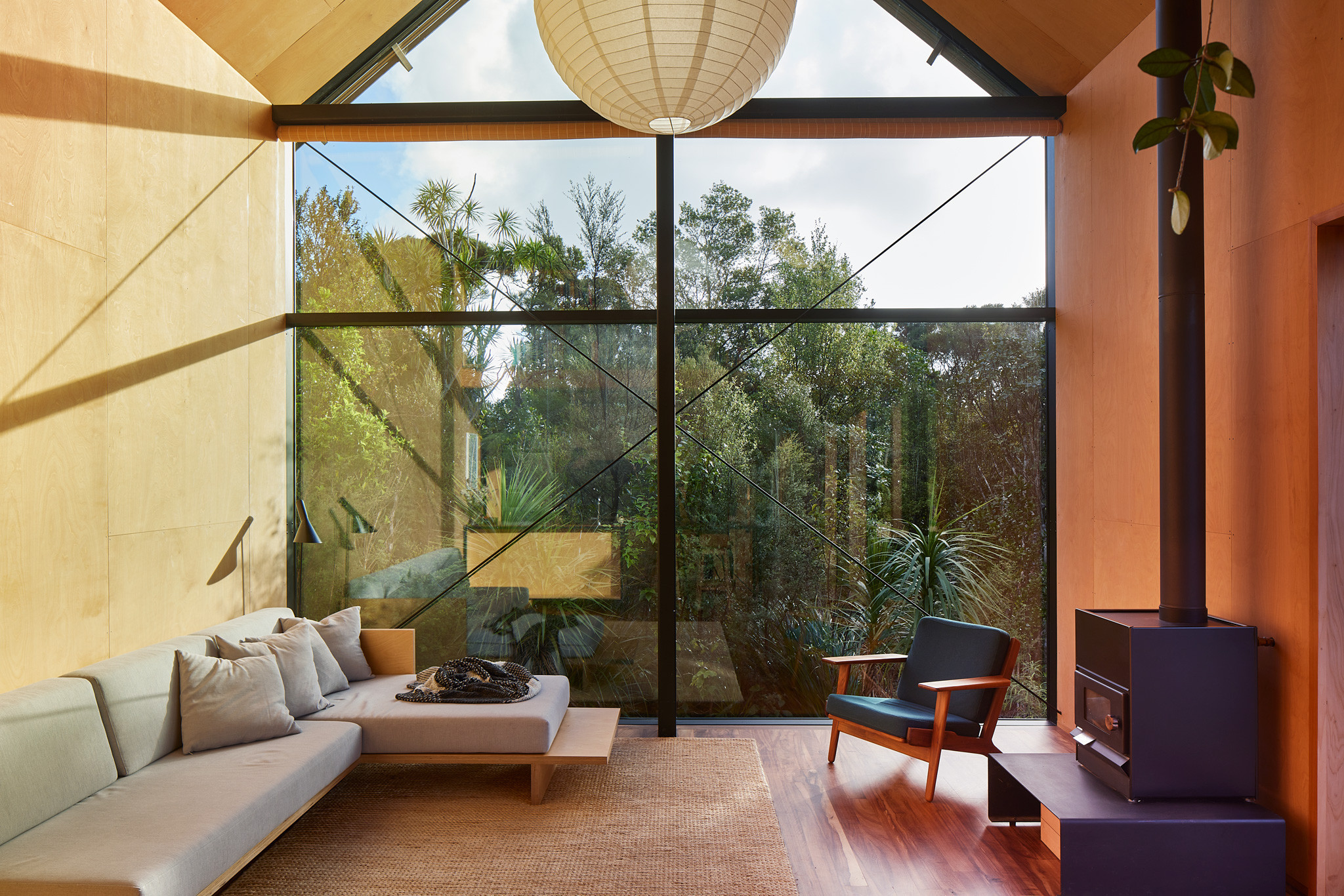 Cosy interior with neutral tones and plush seating, complemented by floor-to-ceiling windows that frame a serene bush landscape