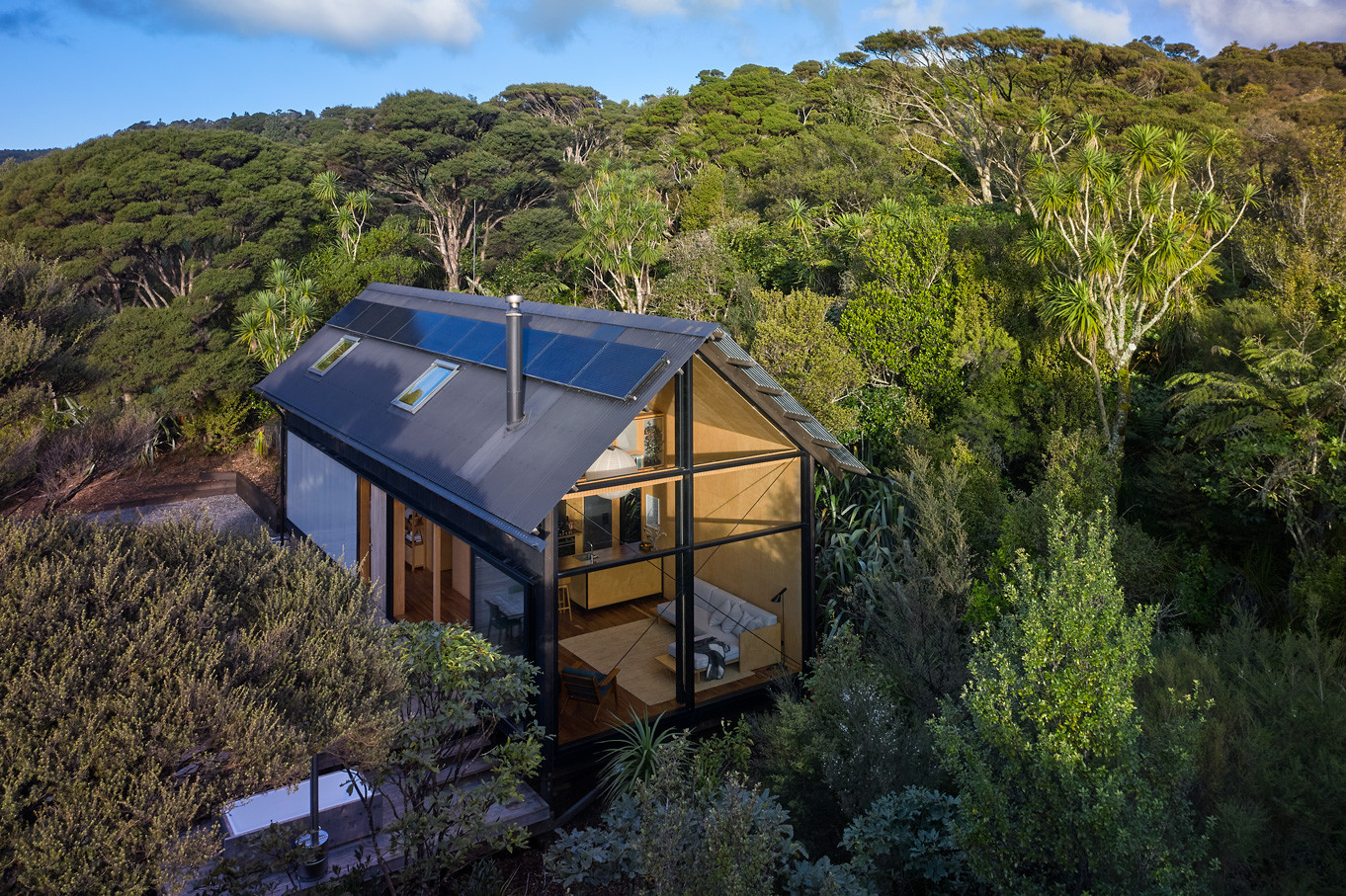 Contemporary house ensconced in nature, boasting a large glass window facade amidst a verdant bush landscape