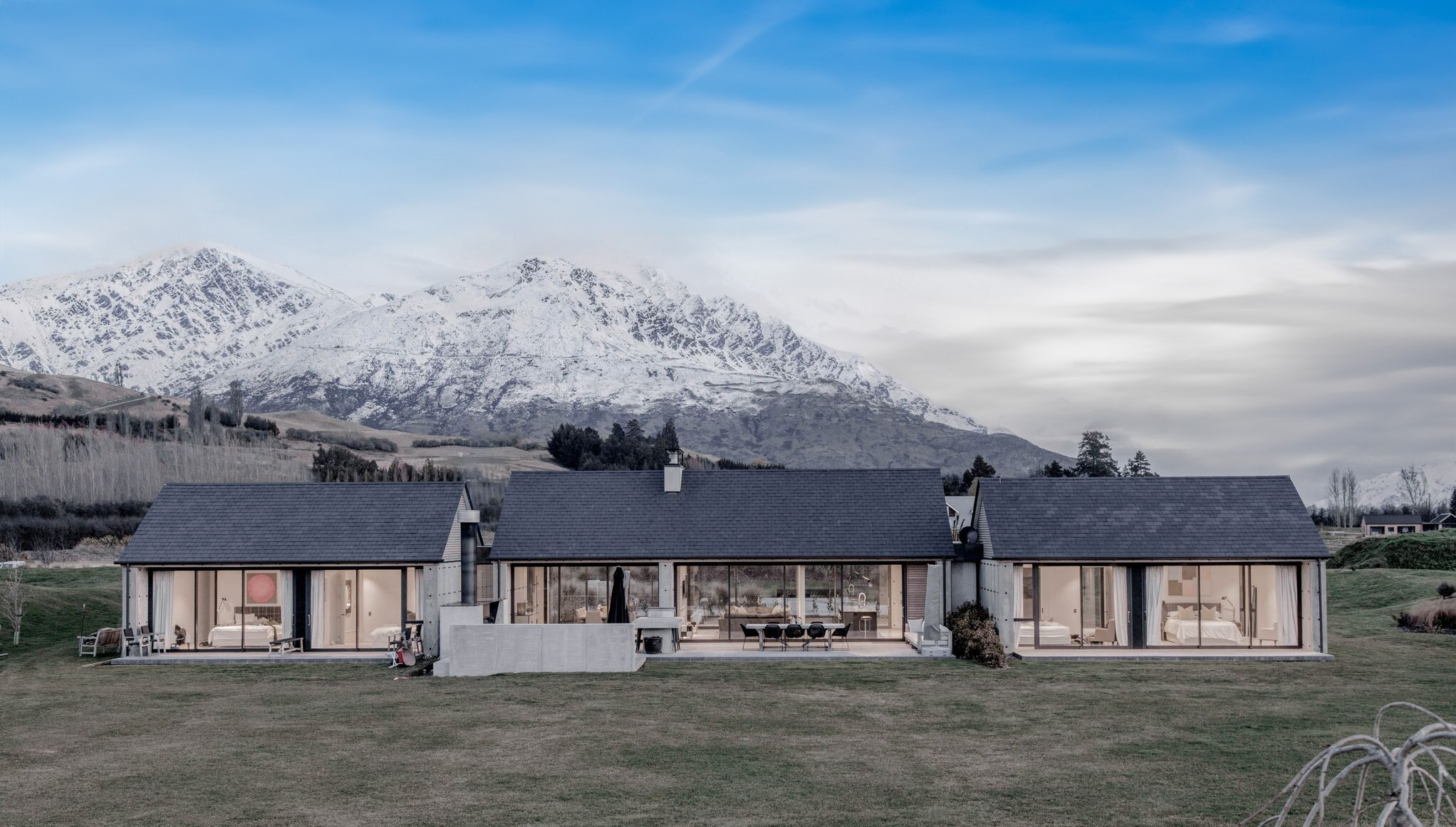 A modern house with mountains in the background, featuring wall-to-ceiling windows and doors