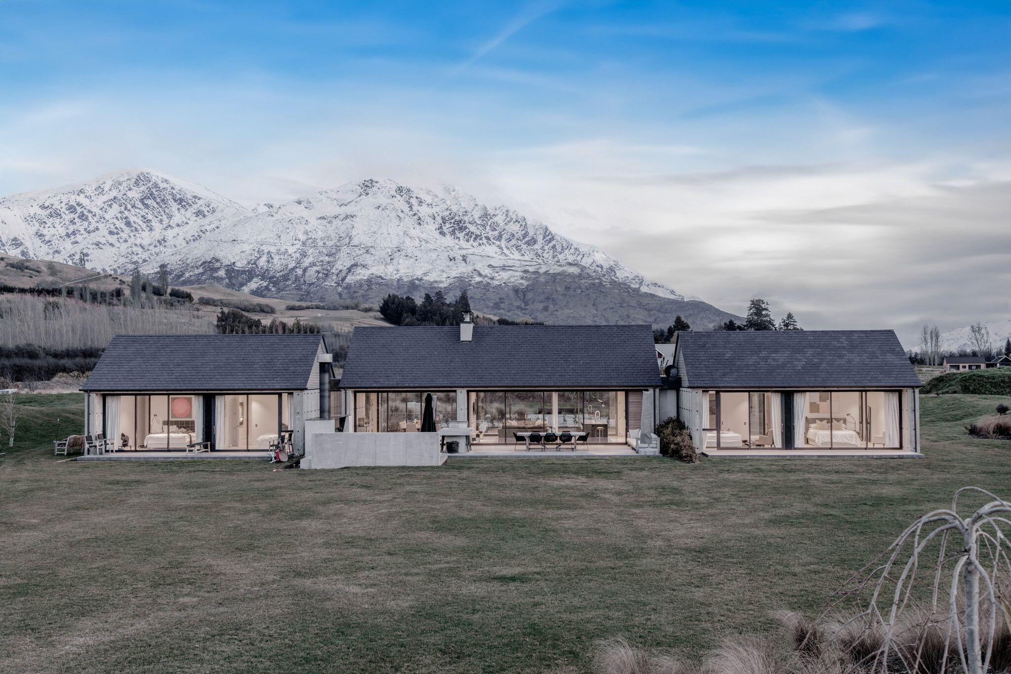 A modern house with mountains in the background, featuring wall-to-ceiling windows and doors