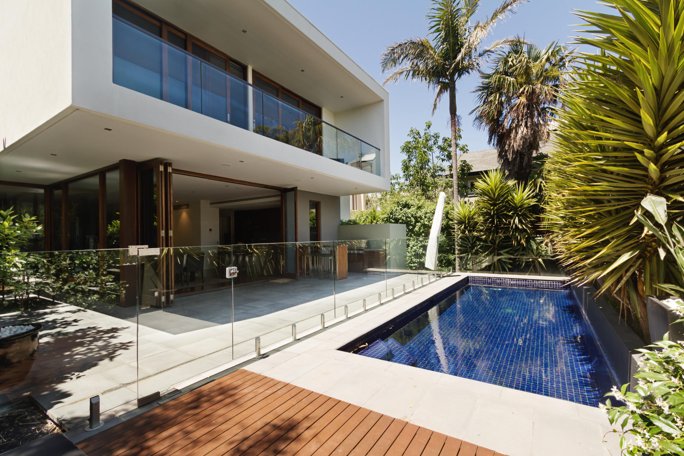 A stylish home with a pool and wooden decking with a frameless glass fence