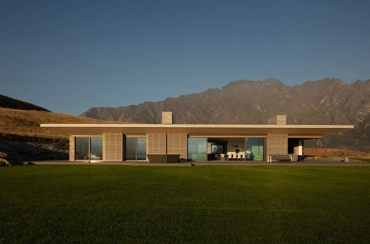 Gorgeous contemporary home featuring glazed glass windows, manicured lawn, and stunning mountain backdrop