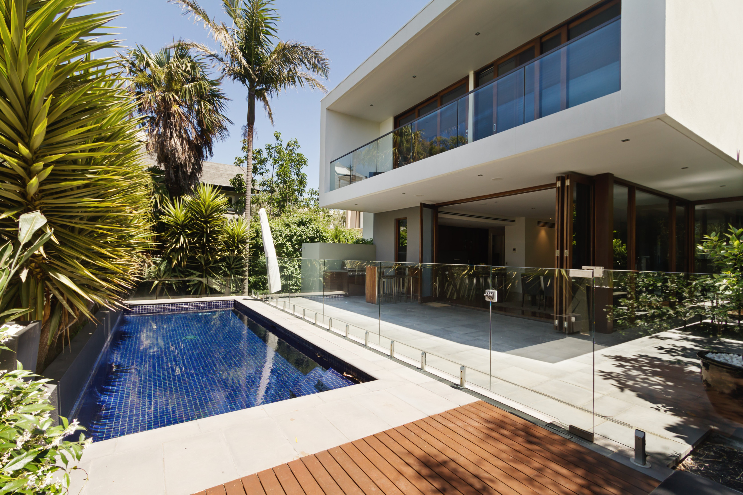 Luxurious private residence with a clear glass balustrade surrounding an inviting blue-tiled swimming pool