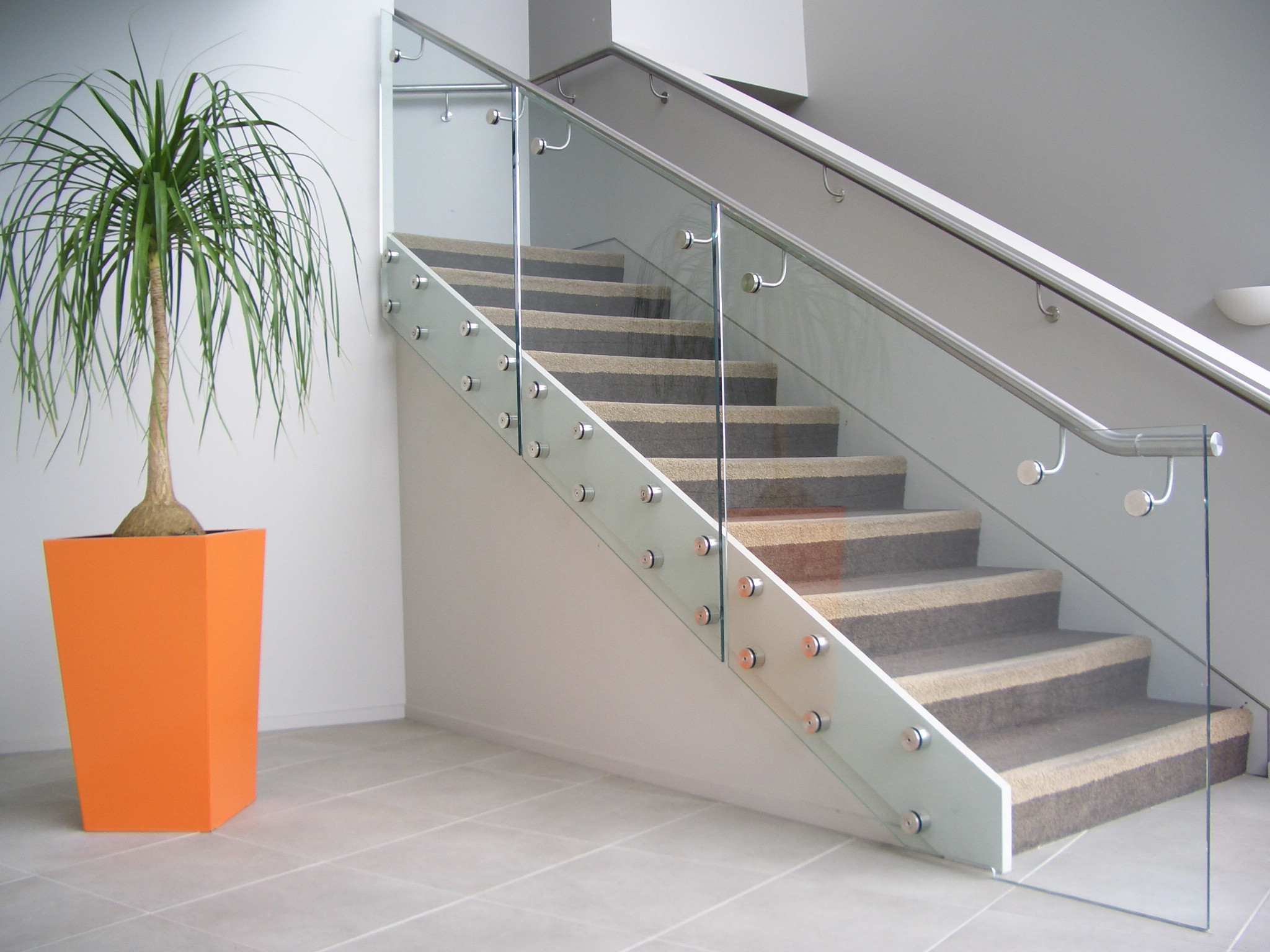 Modern interior staircase with a glass balustrade, with orange pot plant