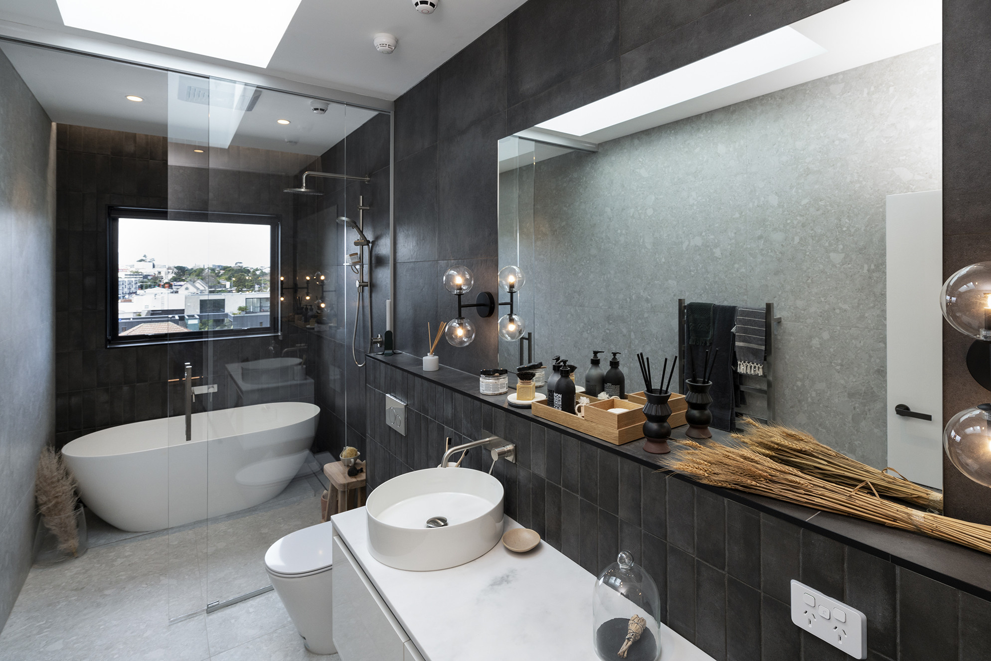 Modern bathroom with a transparent glass shower screen, bath, basin, and black tiled wall