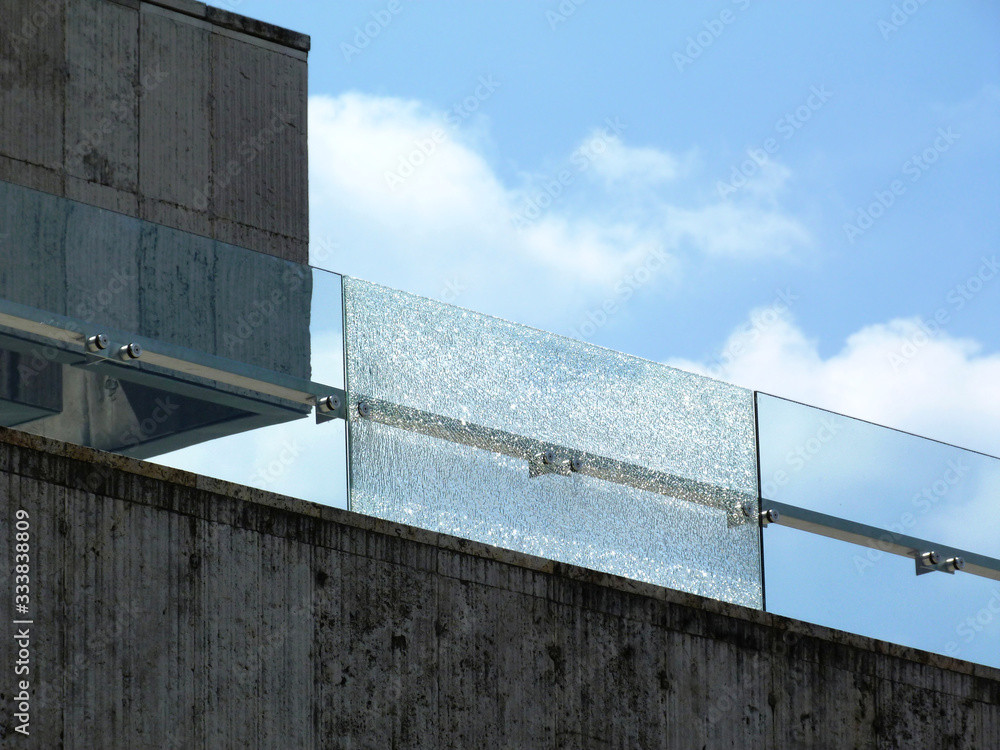 Glass safety railing on rooftop with blue sky in background.