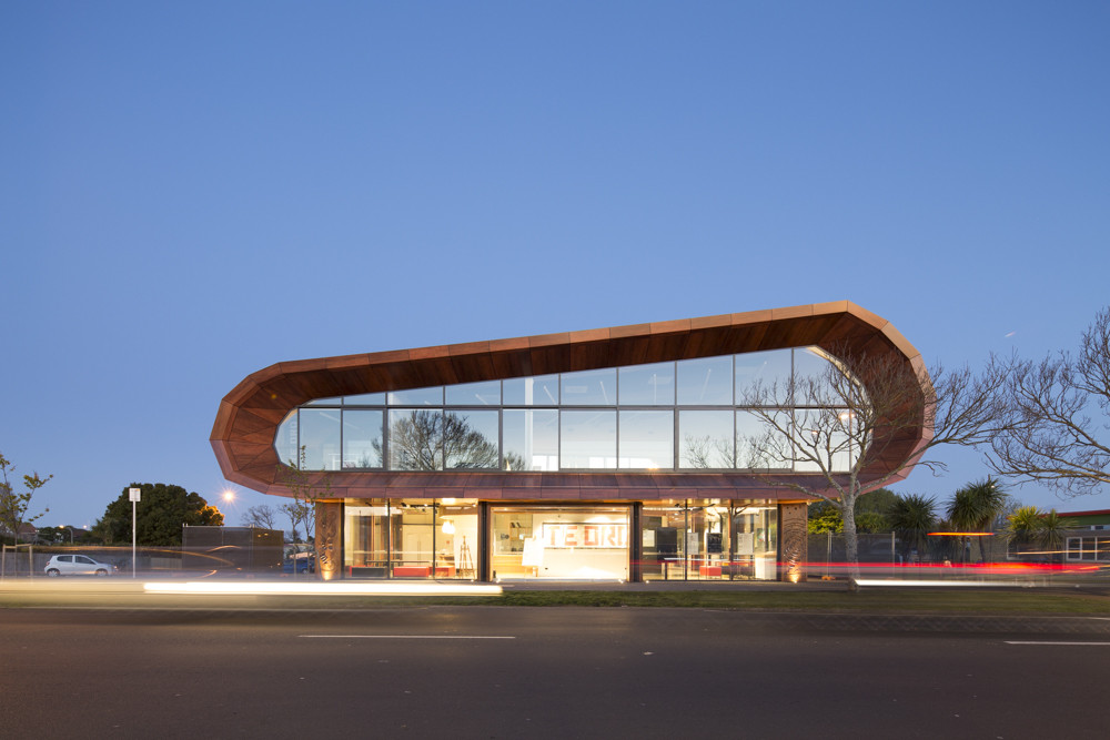 A unique wooden building with a curved shape and big glass windows on the outside