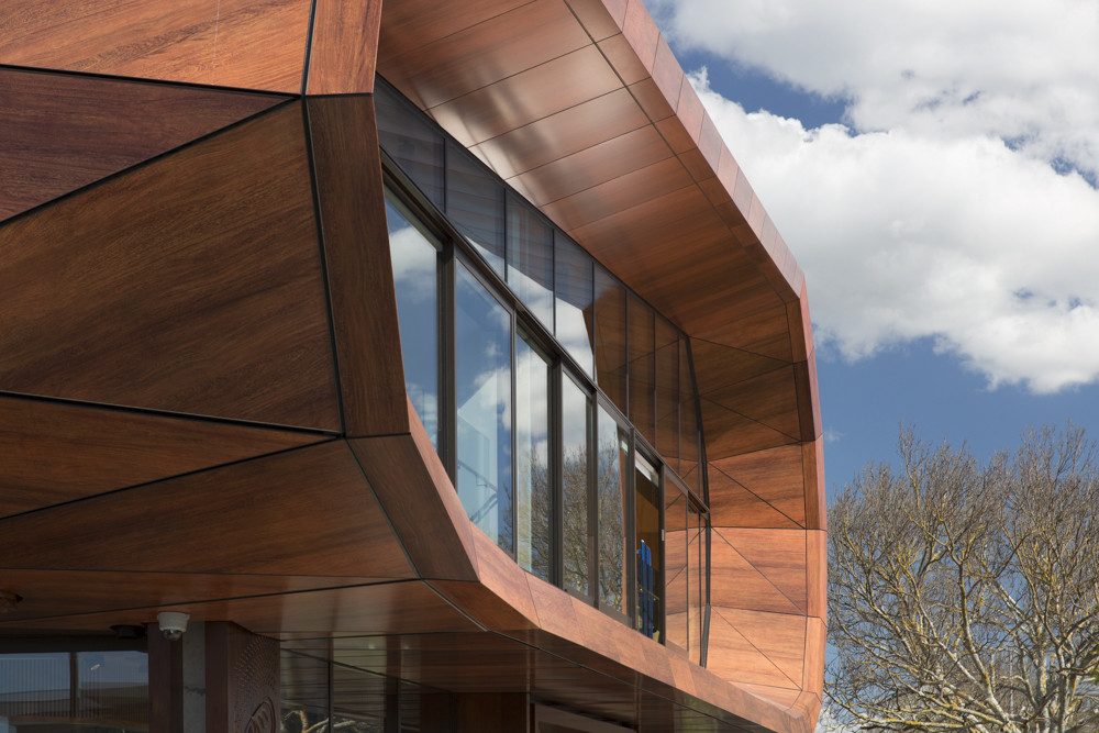 A wooden building showcasing a curved structure and striking glass windows on the outside