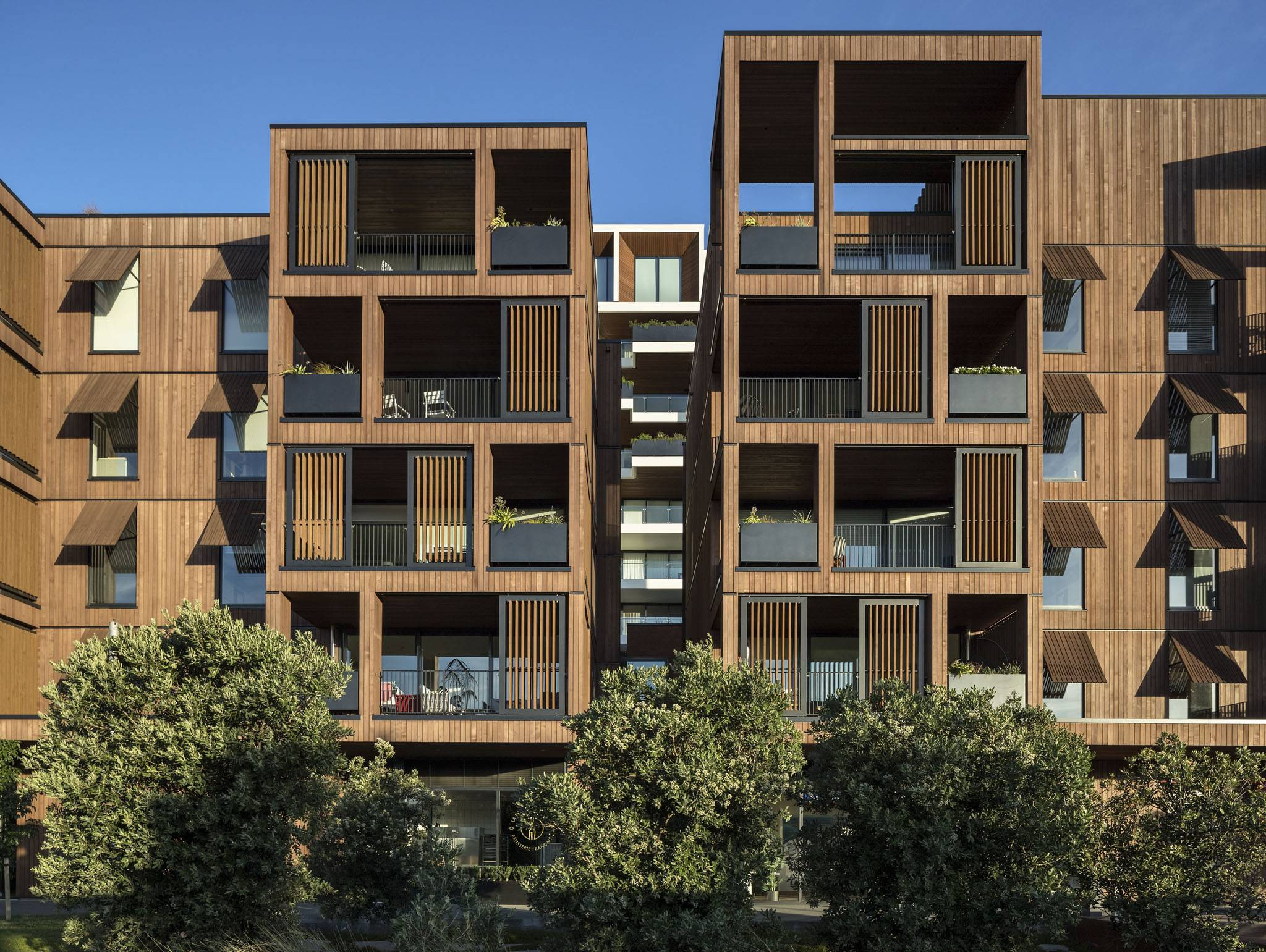 Modern residential building with dark wood paneling and clear glass balustrades