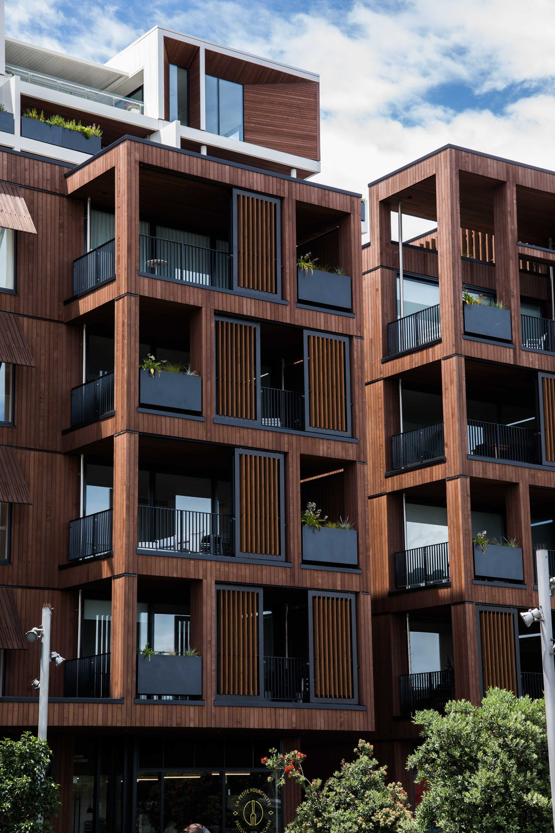 Wood-finished apartment building with glass balustrades and recessed balconies