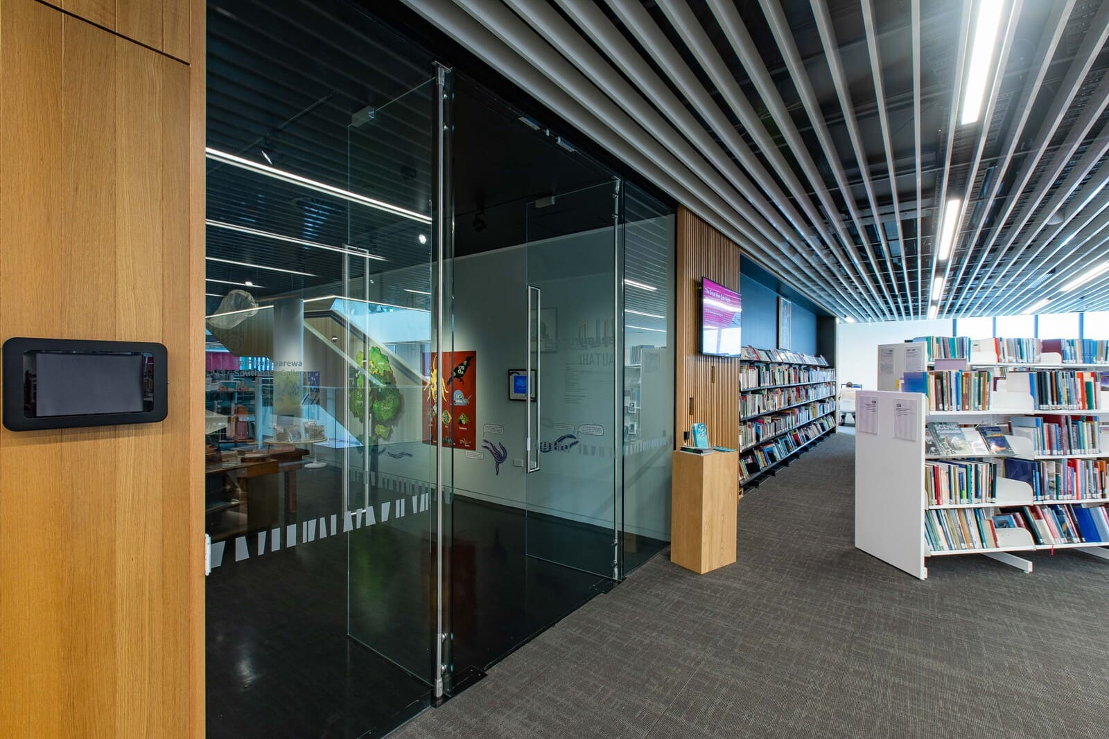 A modern library with glass doors, a unique ceiling, and shelves filled with books