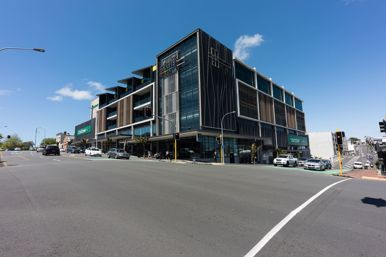 A modern building with parked cars on the street, showcasing a glass patterned exterior with highlighted panels and facade