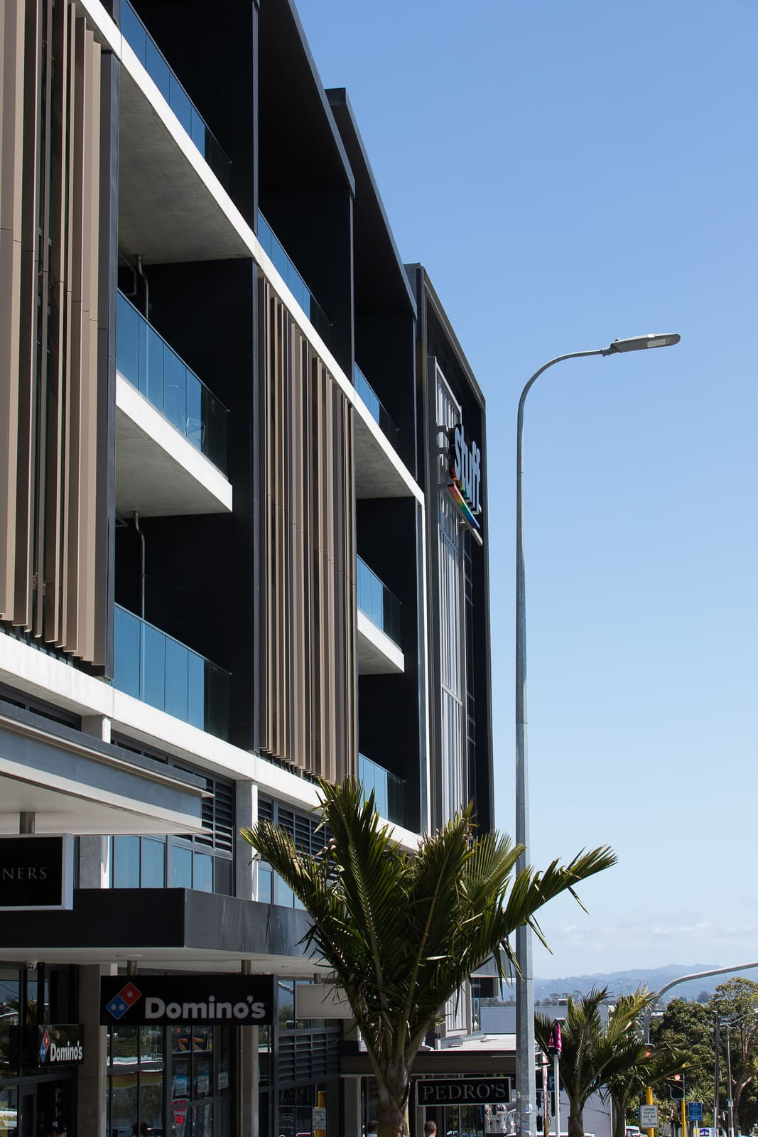 A sleek building with cars parked outside, boasting a glass patterned exterior and highlighted panels and facade