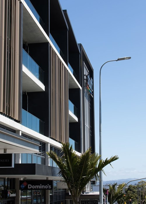 A sleek building with cars parked outside, boasting a glass patterned exterior and highlighted panels and facade