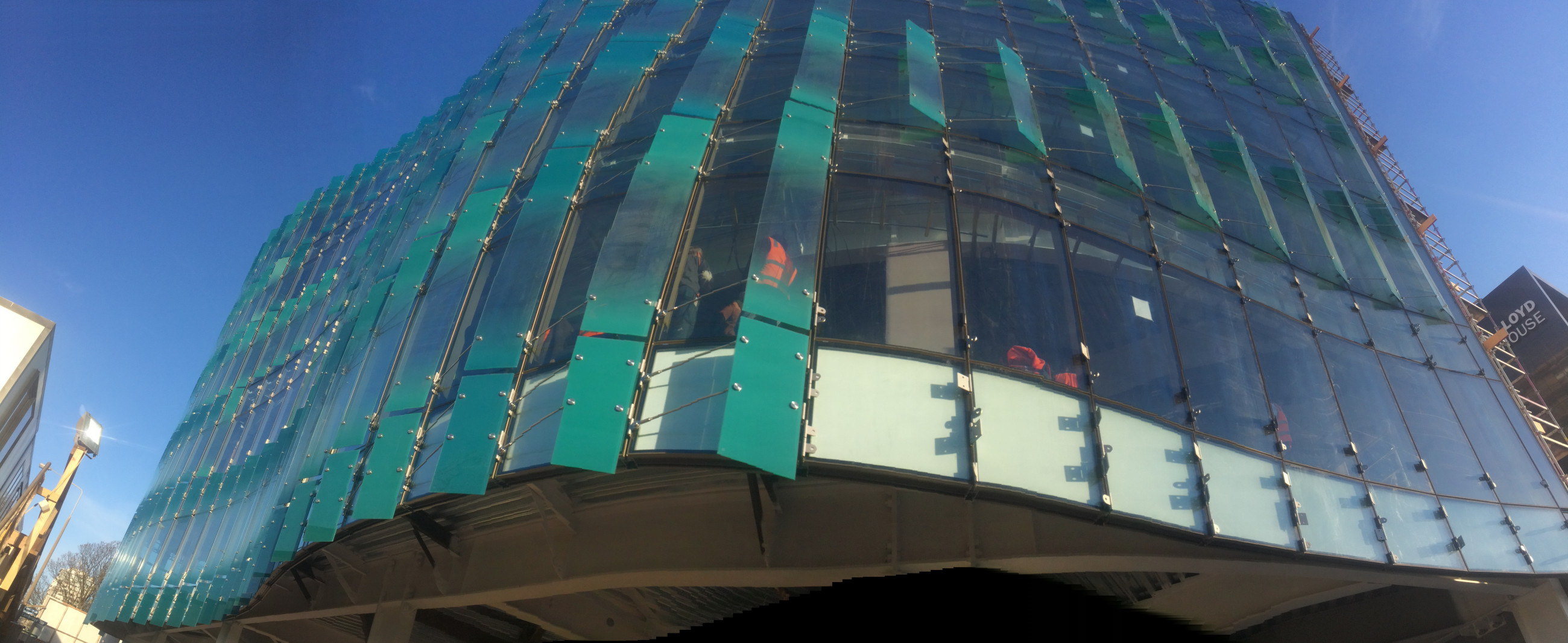 A modern building with glass windows and a highlighted facade against a beautiful blue sky.