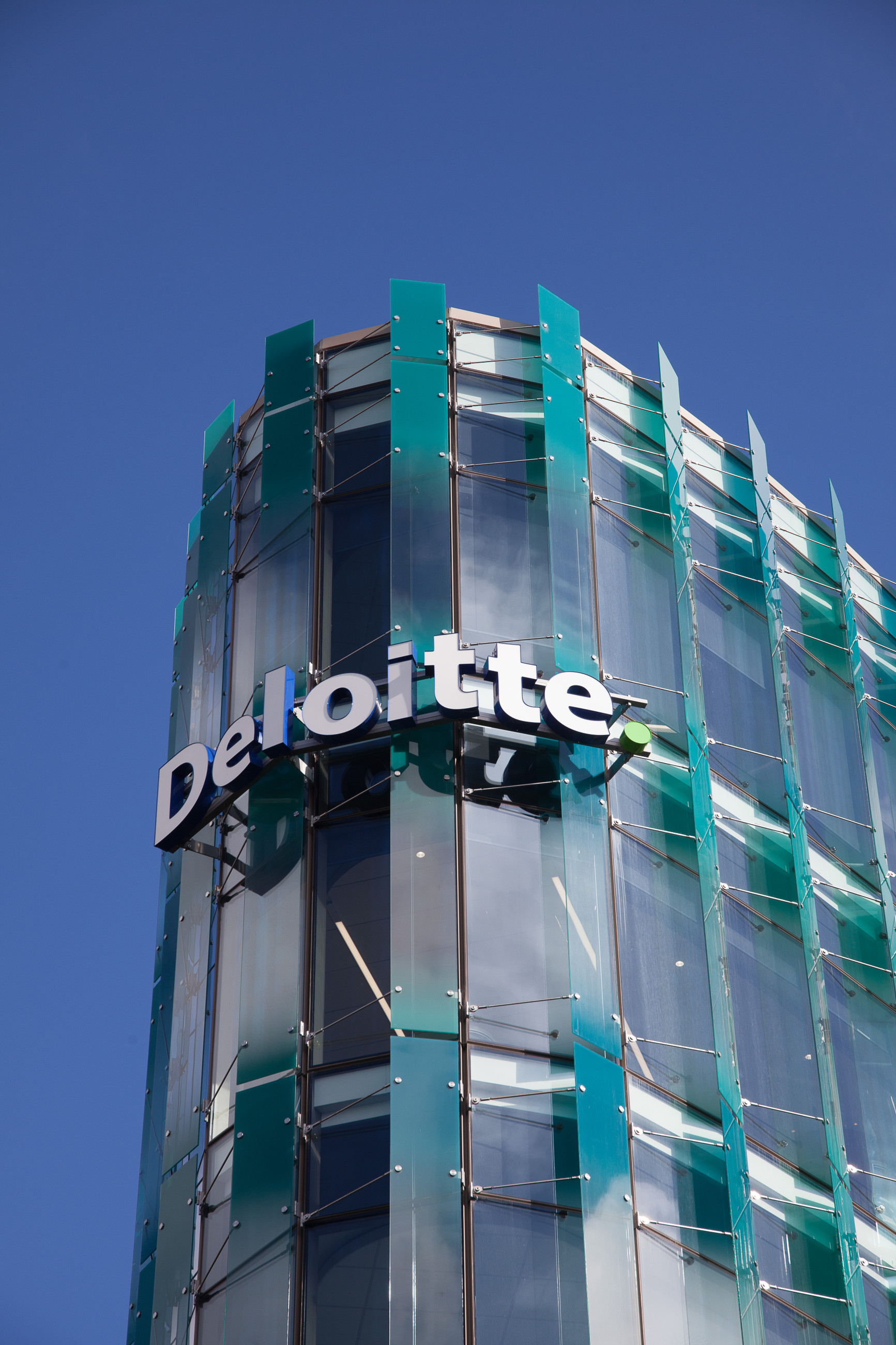 Modern building with glass windows and highlighted facade with deloitte words on it