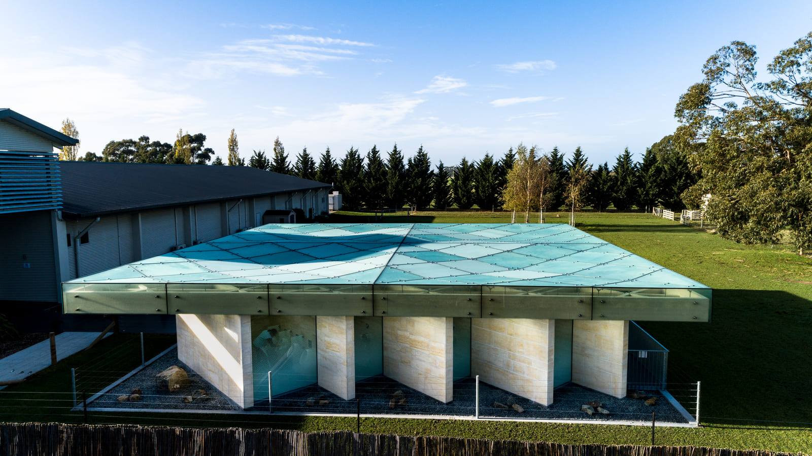 Glass panels shine on a light brick building, surrounded by green grass