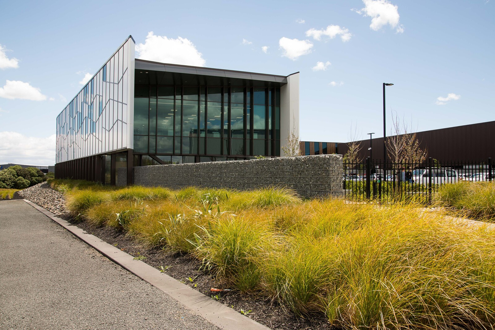Large building with patterned glass exterior contrasting with white panels, in front of grass bushes