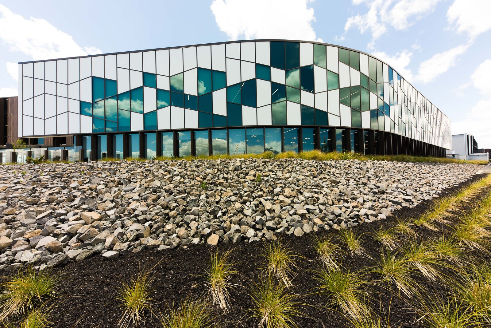 Modern building with patterned glass walls and white panels, surrounded by green bushes