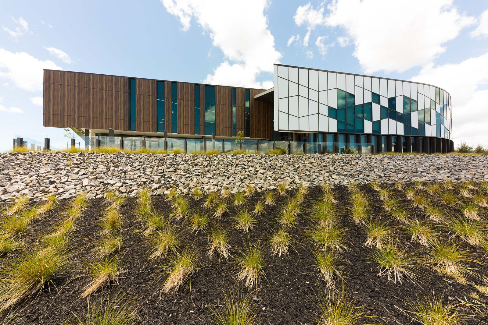 Modern building with patterned glass walls and white panels, surrounded by green bushes