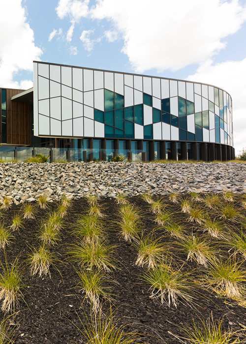 Contemporary structure showcasing glass windows, white panels, and a backdrop of green bushes