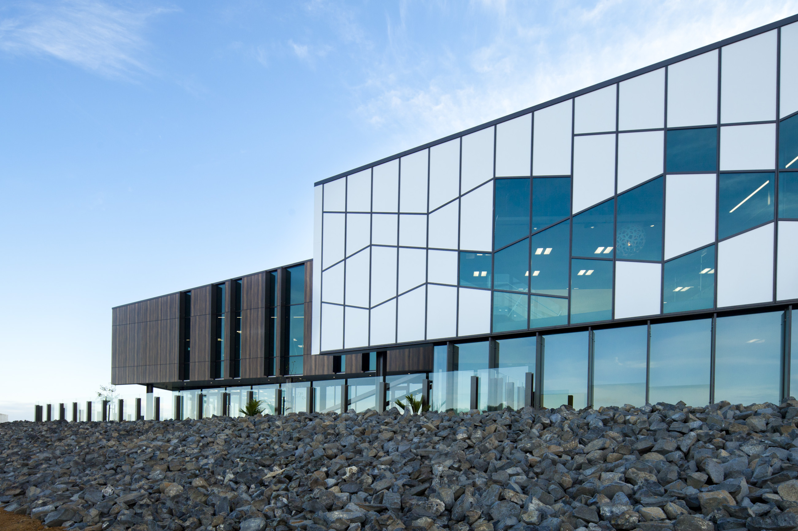 Building with intricate glass exterior, white panels, and rocks in the foreground