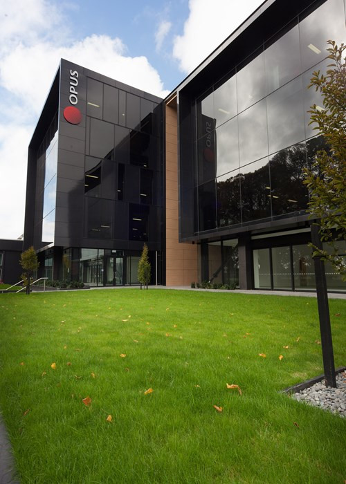 Opus building with dark tinted windows, set amidst lush green grass