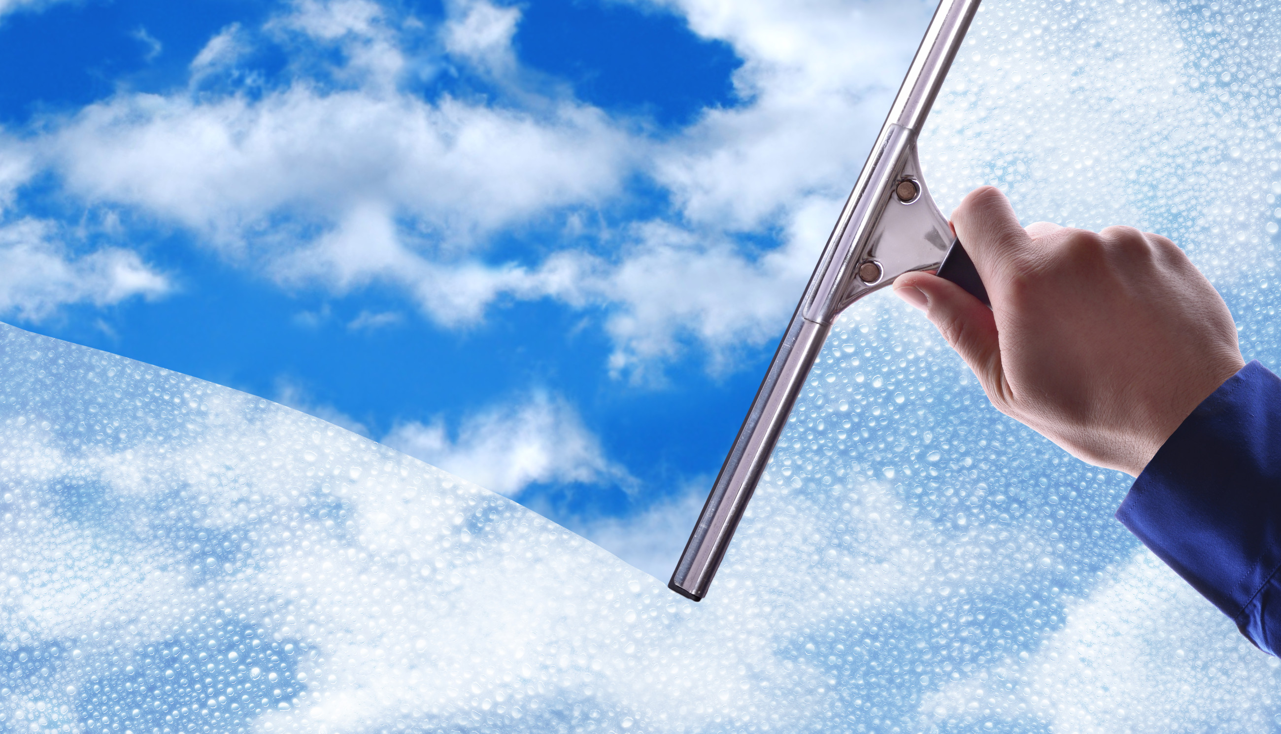 Man cleaning a Metro Glass window with cloudy blue sky in background