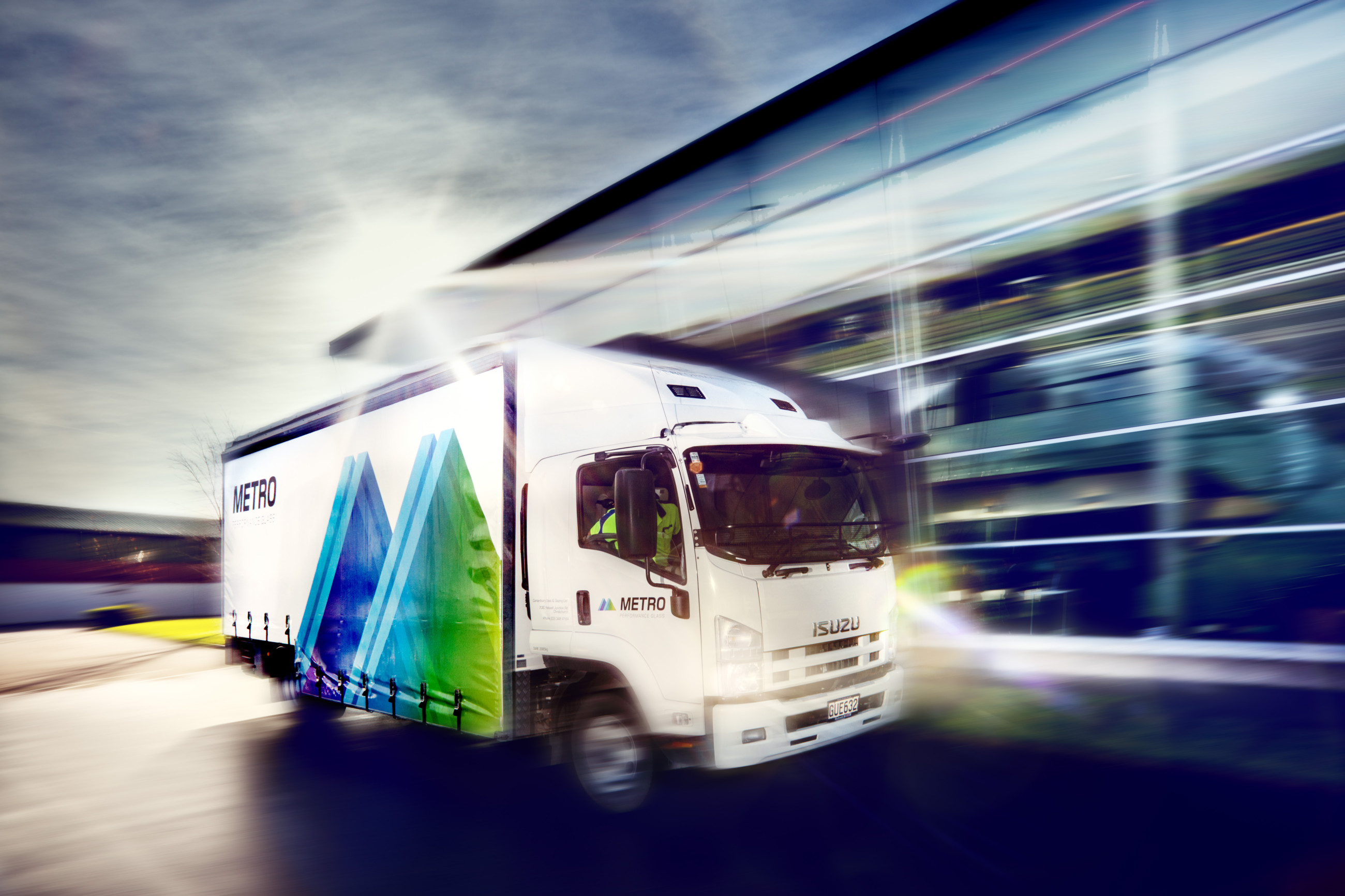 A Metro glass truck driving down the road with a building in the background