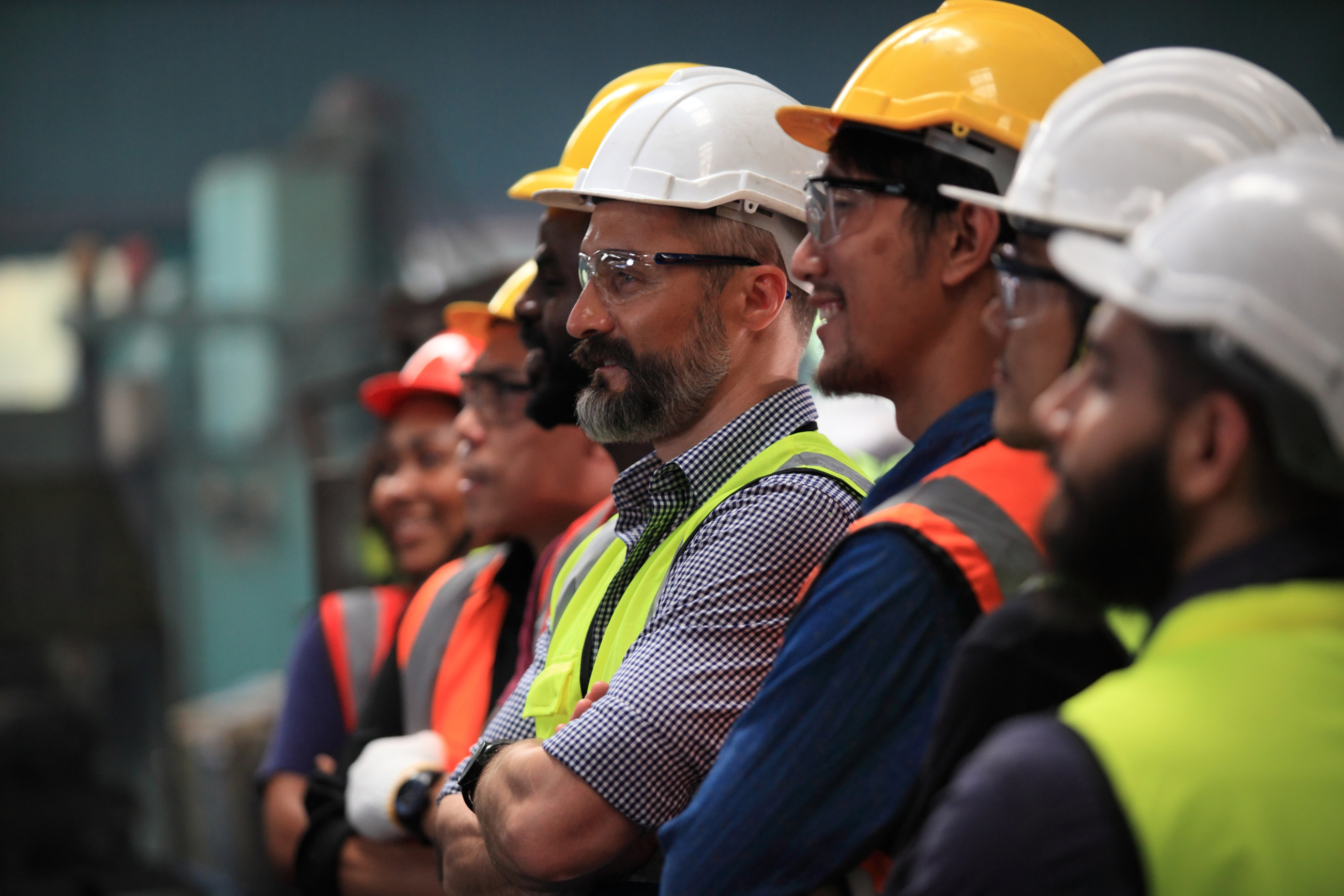 Men in safety hats standing with arms folded in a row