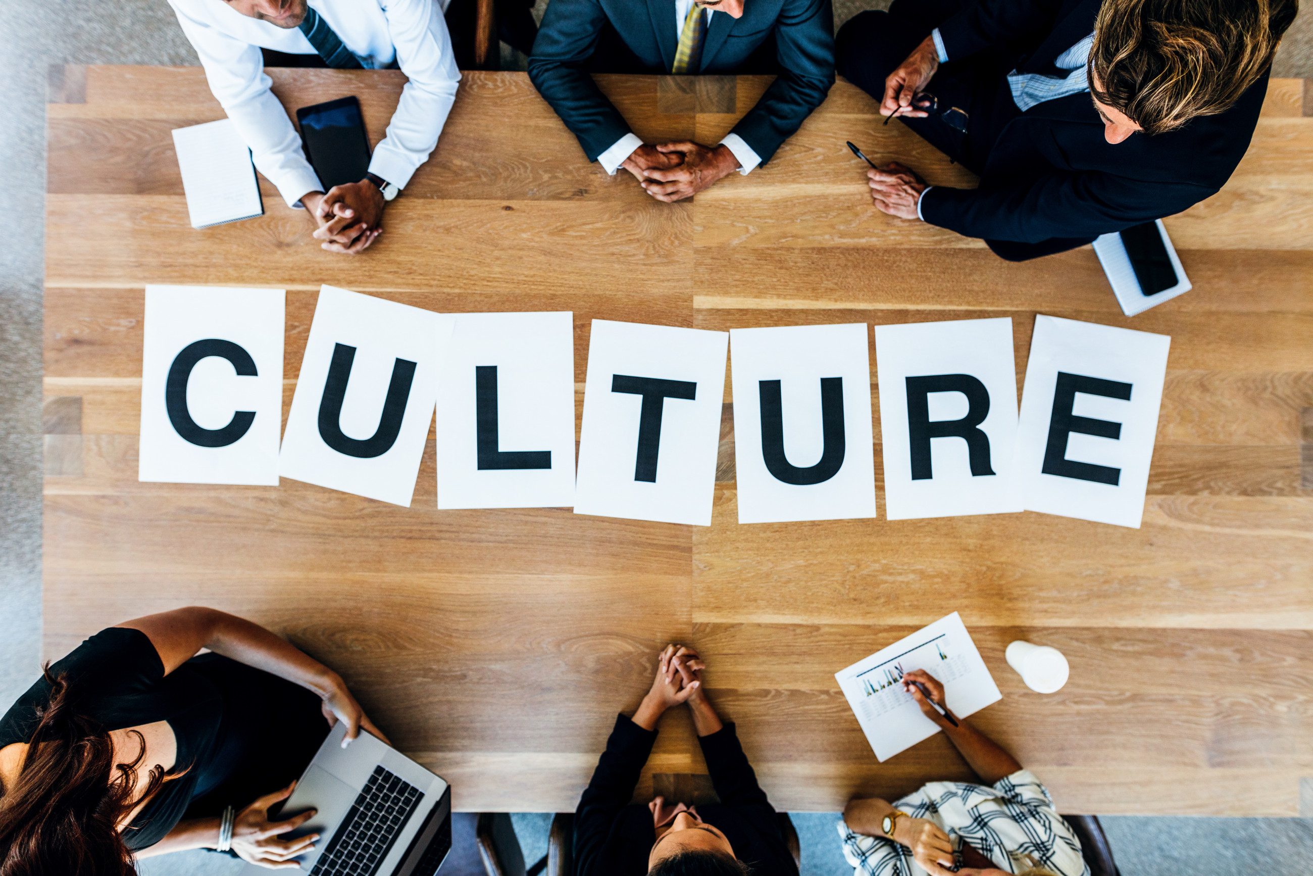 People sitting at a table with white papers spelling 'culture' in large letters